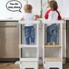 Two children are standing at the kitchen sink.  Both are in Explore N Store Learning Towers.  One child says 