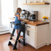 A child stands at the kitchen counter in the Learn 'N Fold Learning Tower in Natural Color.