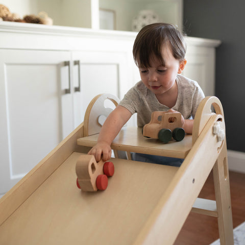 A young boy is playing with wooden trucks on the 2-in-1 Folding Learn N Slide.