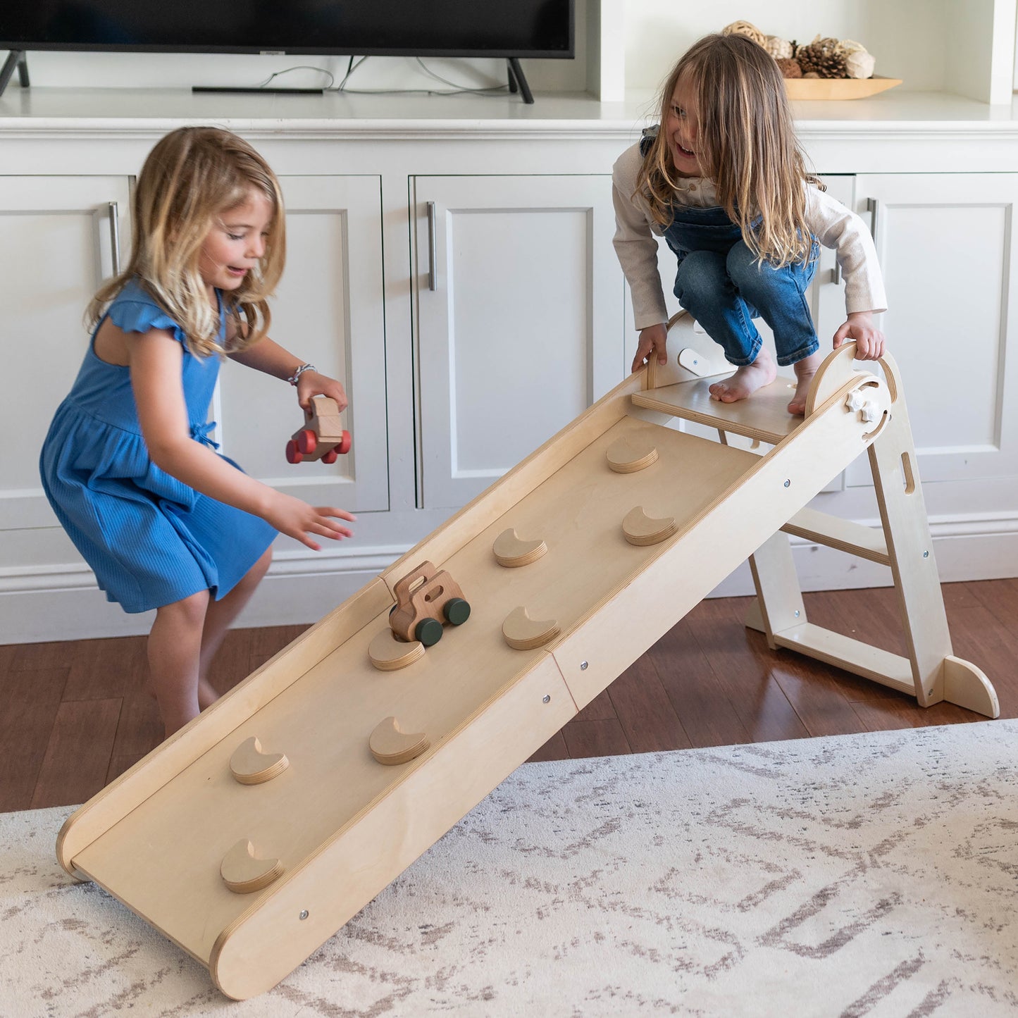 Two young girls are playing with wooden cars on the 2-in-1 Folding Learn N Slide Ramp.