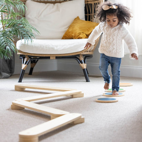 A little girl is walking on the color Stepping Stones next to the Balance Beam.