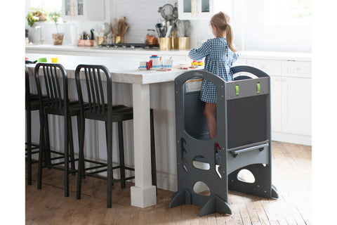 A young girl stands at the kitchen counter in the Limited Edition Learning Tower in Earl Grey color. 