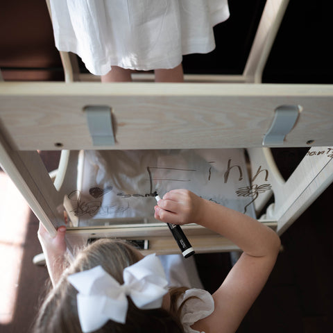 A close up of a young girl writing on the plexiglass panel of the Chef Series Learning Tower.