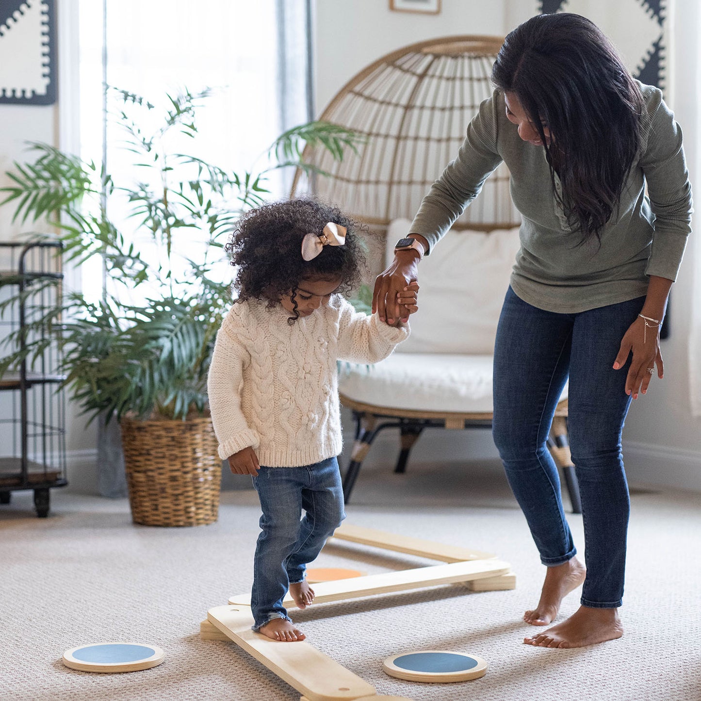 A little girl is walking on the balance beam of the Learn 'N Balance Set.  Her Mom is holding her hand.